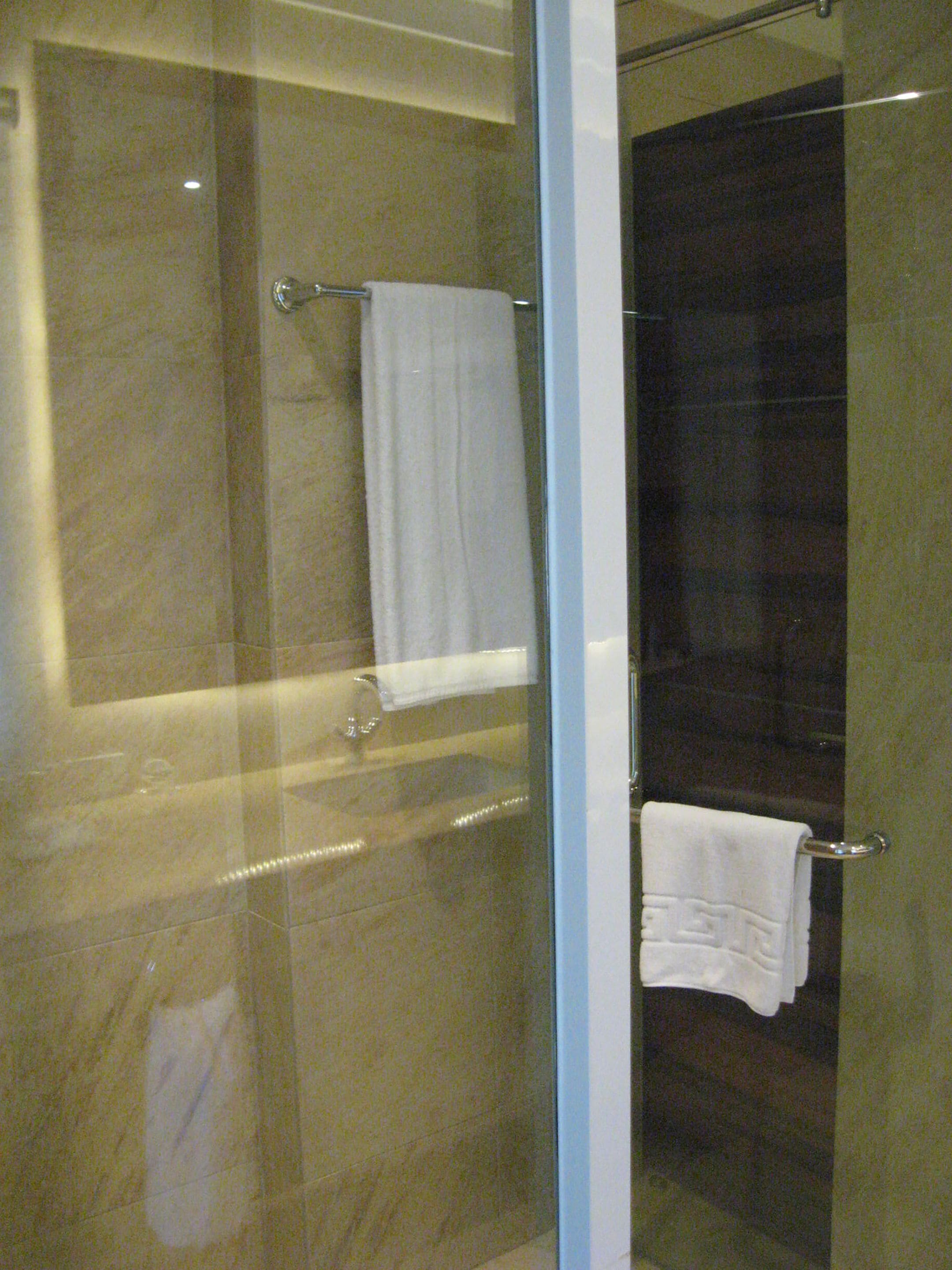 A glass-enclosed shower area with a dark tiled wall and a white towel hanging on a metal rack.