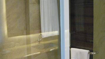 A glass-enclosed shower area with a dark tiled wall and a white towel hanging on a metal rack.