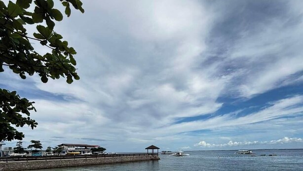 Una escena costera con un muelle que se adentra en el agua, una playa arenosa y un cielo despejado.