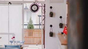 A cafe interior with a clock, blue chairs, and hanging planters. - MB City Hotel (Izmir)