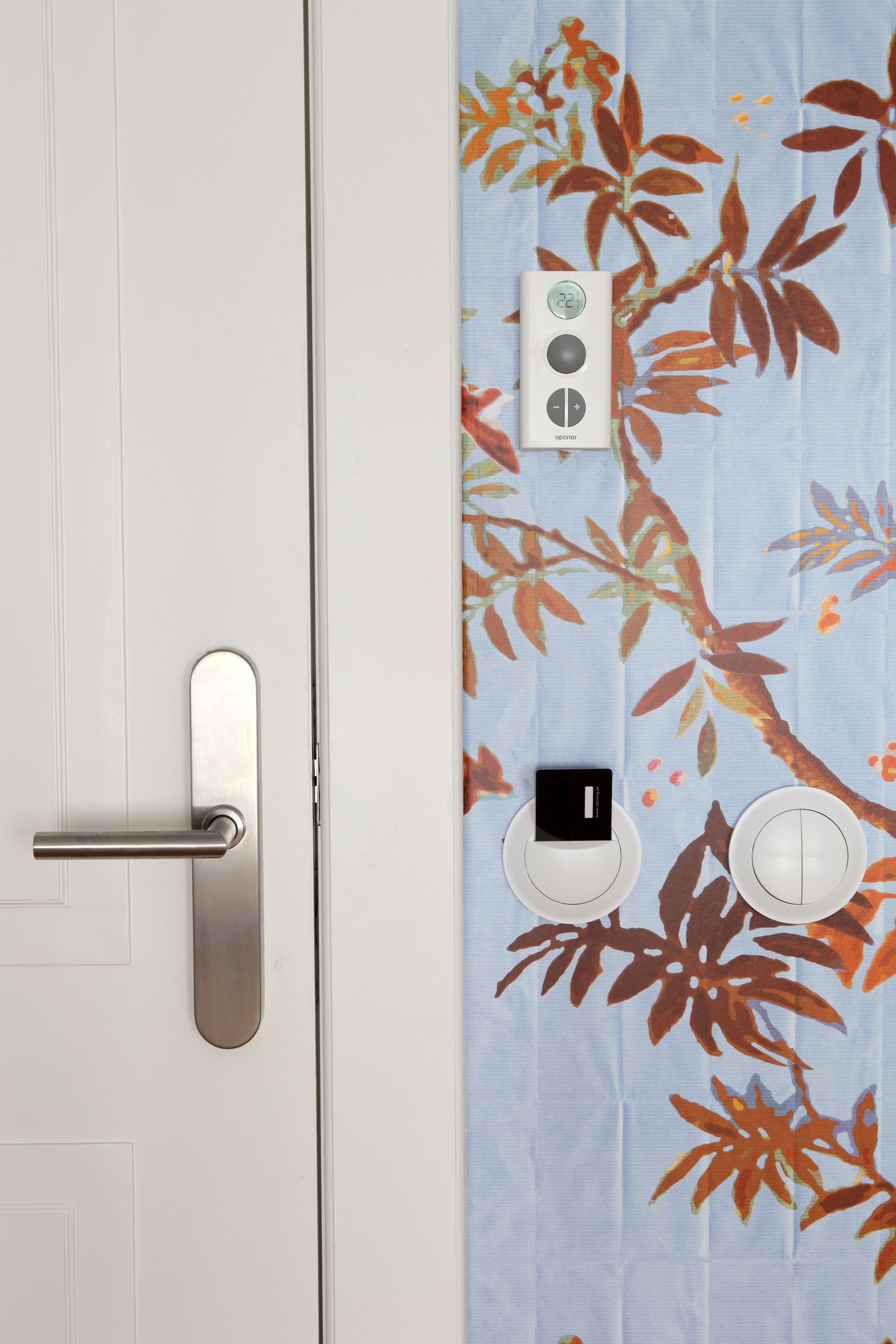 A bathroom with a white door, a metallic handle, a towel dispenser, and a toilet paper holder.