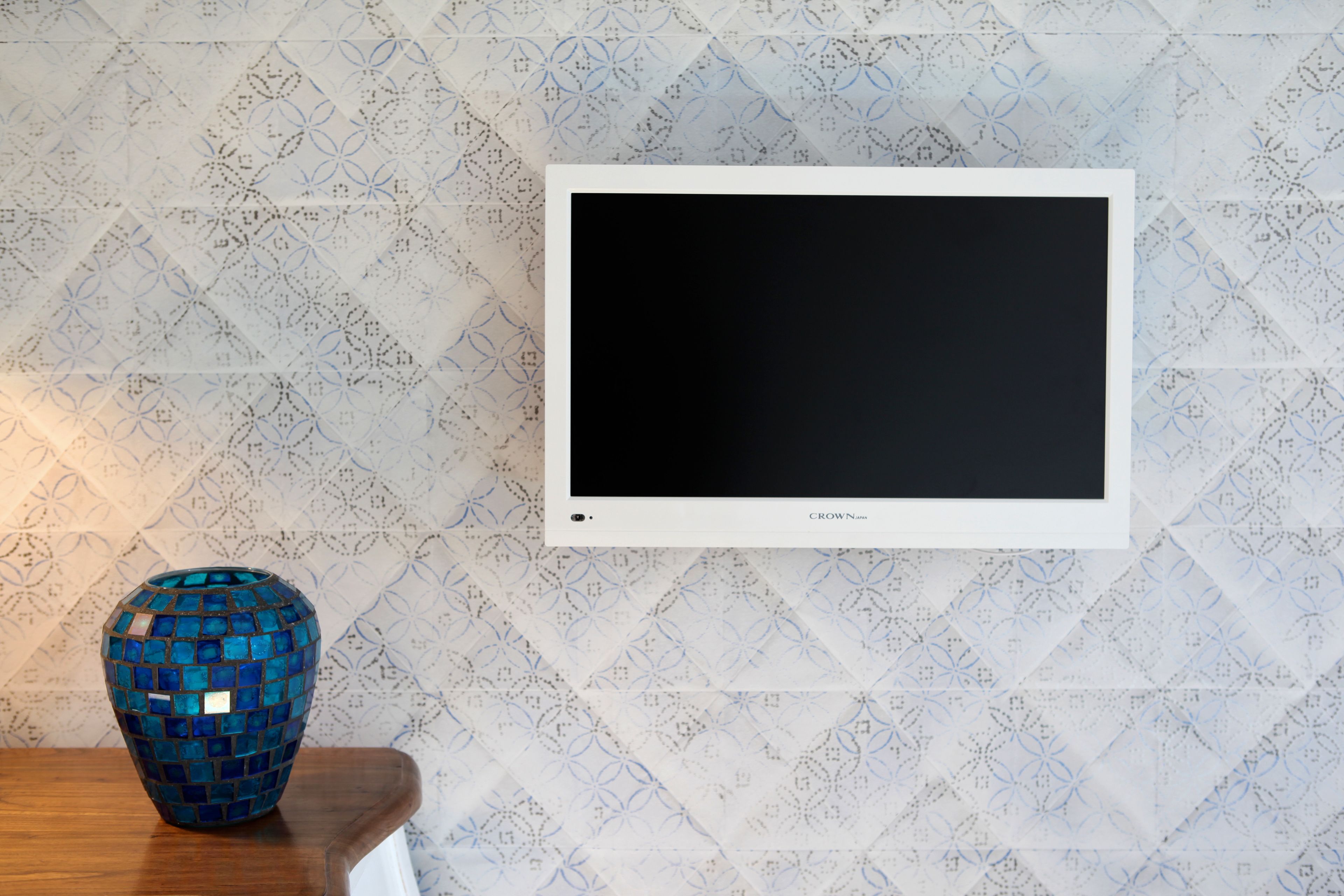 Televisão presa na parede com papel de parede estampado em padrão geométrico.