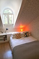 Un dormitorio con cama, escritorio, lámpara y ventana.