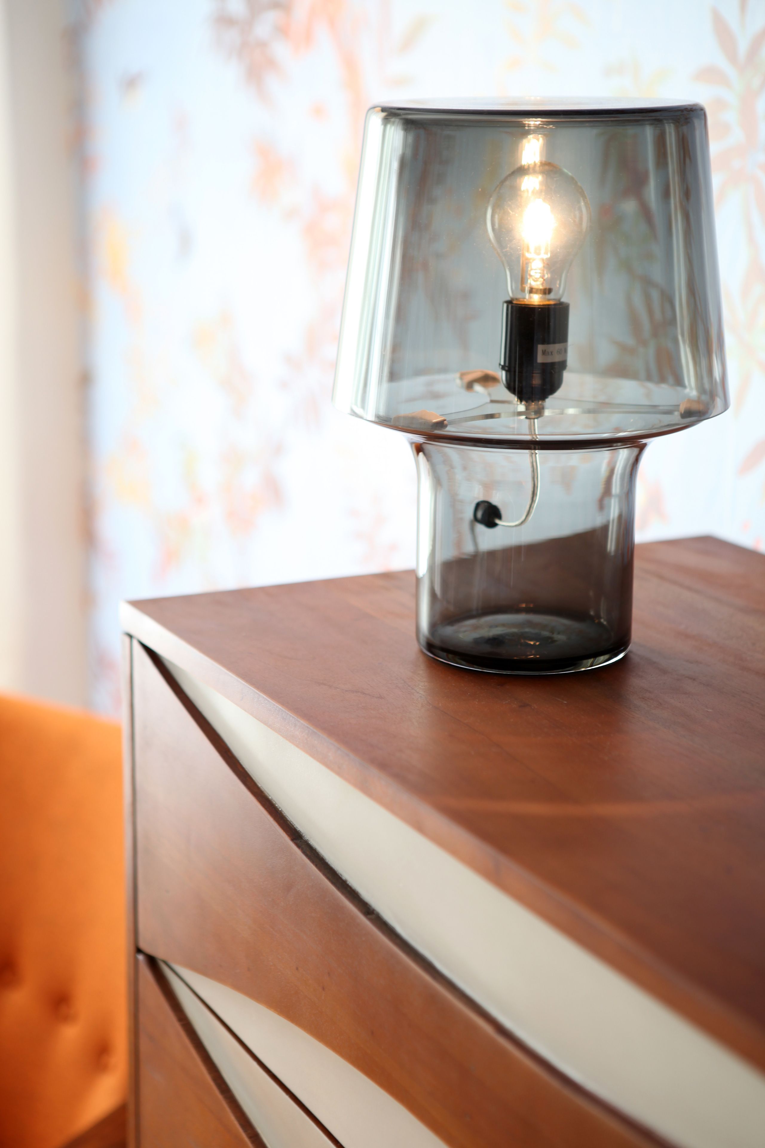 A clear glass lamp with a visible light bulb on a wooden surface.