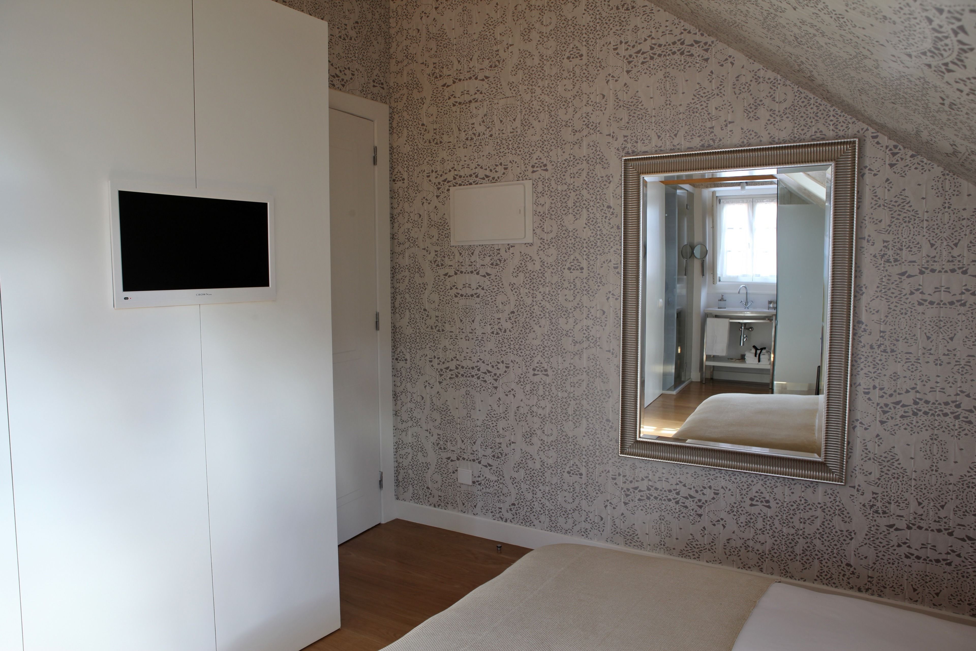 Een slaapkamer met een grote spiegel, een flatscreen televisie en een behang met een patroon.