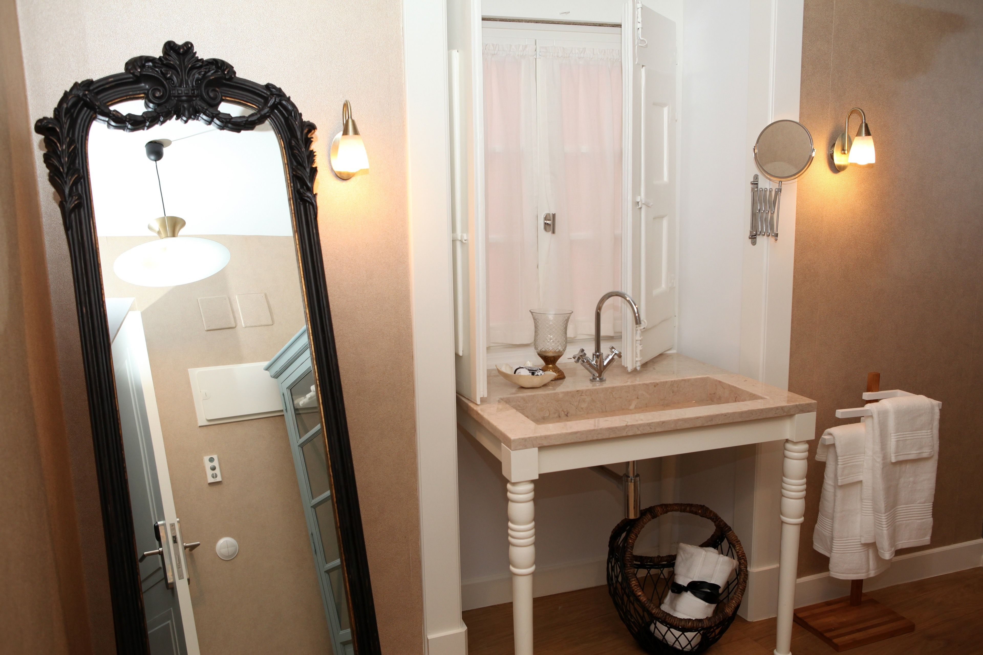 A bathroom with a large ornate mirror, a sink with a towel rack, and a wall-mounted light fixture.