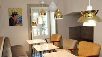 Un intérieur moderne avec un canapé, deux tables et des chaises. Un tableau orne le mur et une porte donne sur l’extérieur.