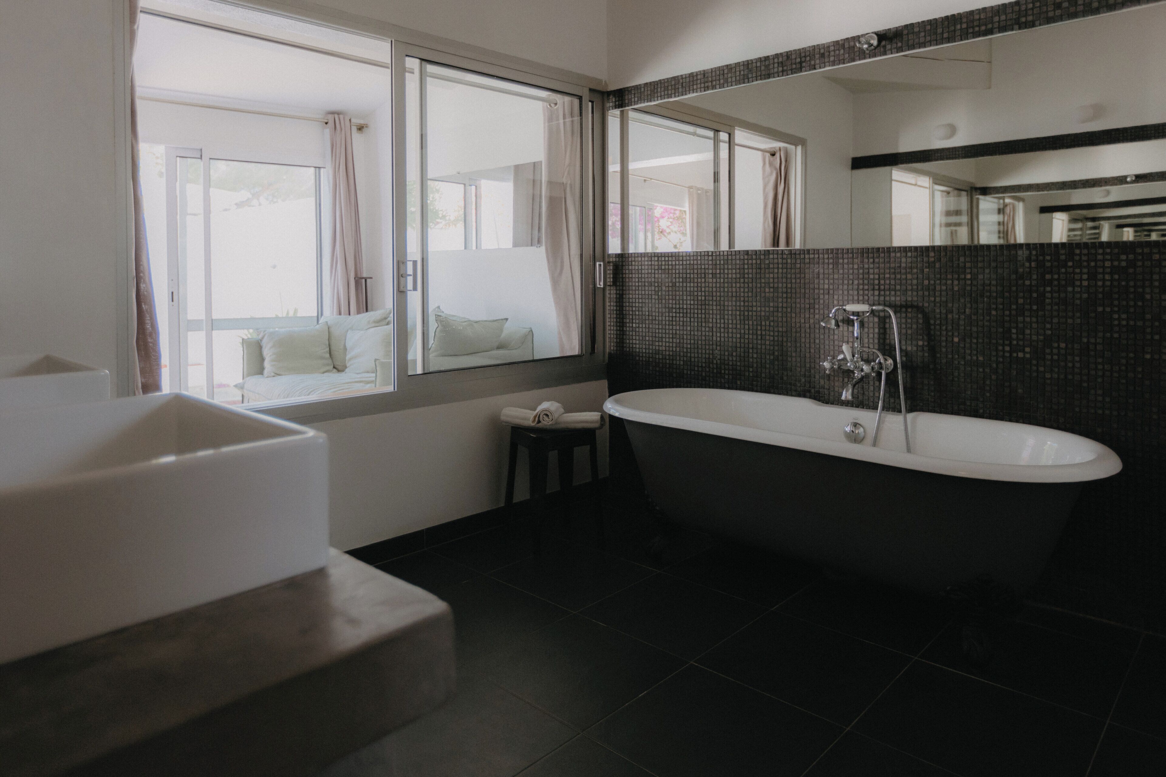 Ein modernes Badezimmer mit einer freistehenden Badewanne, einem Fenster mit Vorhängen und einem großen Spiegel.