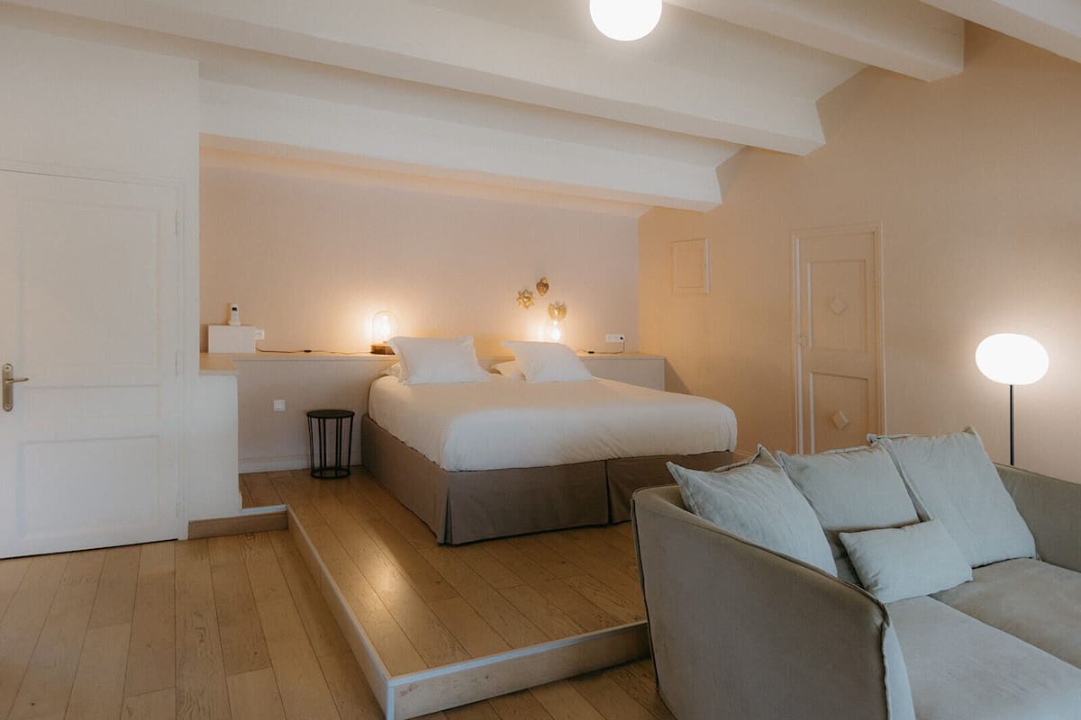 A bedroom with a bed, bedside table, lamp, and a sofa.