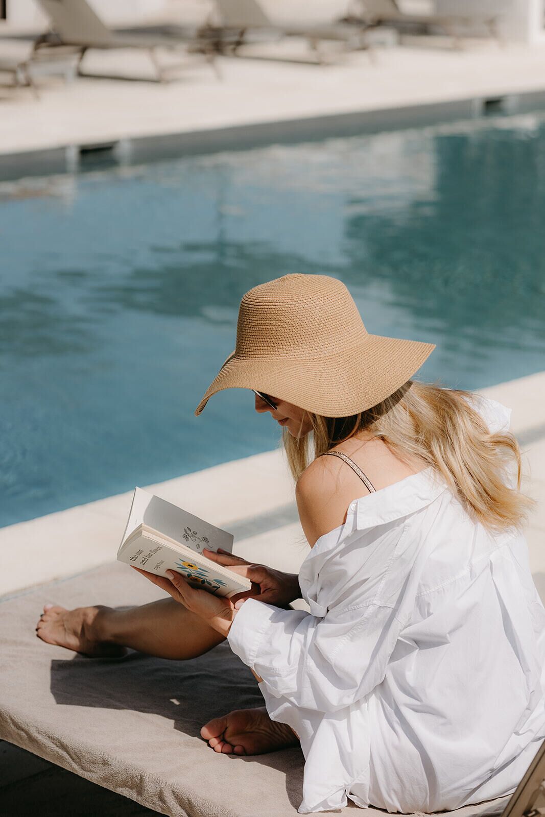 A person sitting by a poolside reading a book.