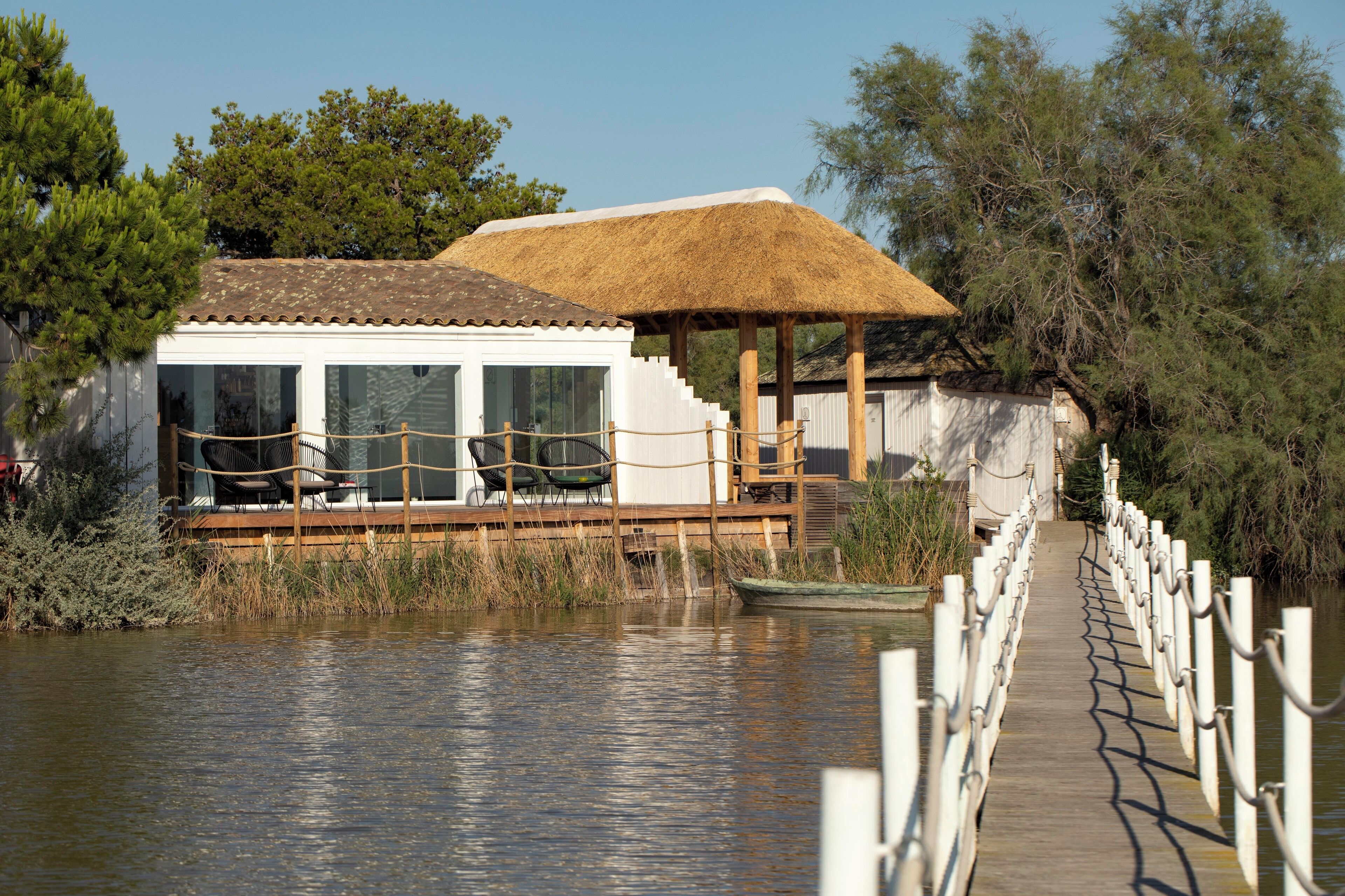Un bâtiment situé au bord de la rivière, doté d’une terrasse en bois, d’un toit de chaume et offrant une vue sur l’eau.