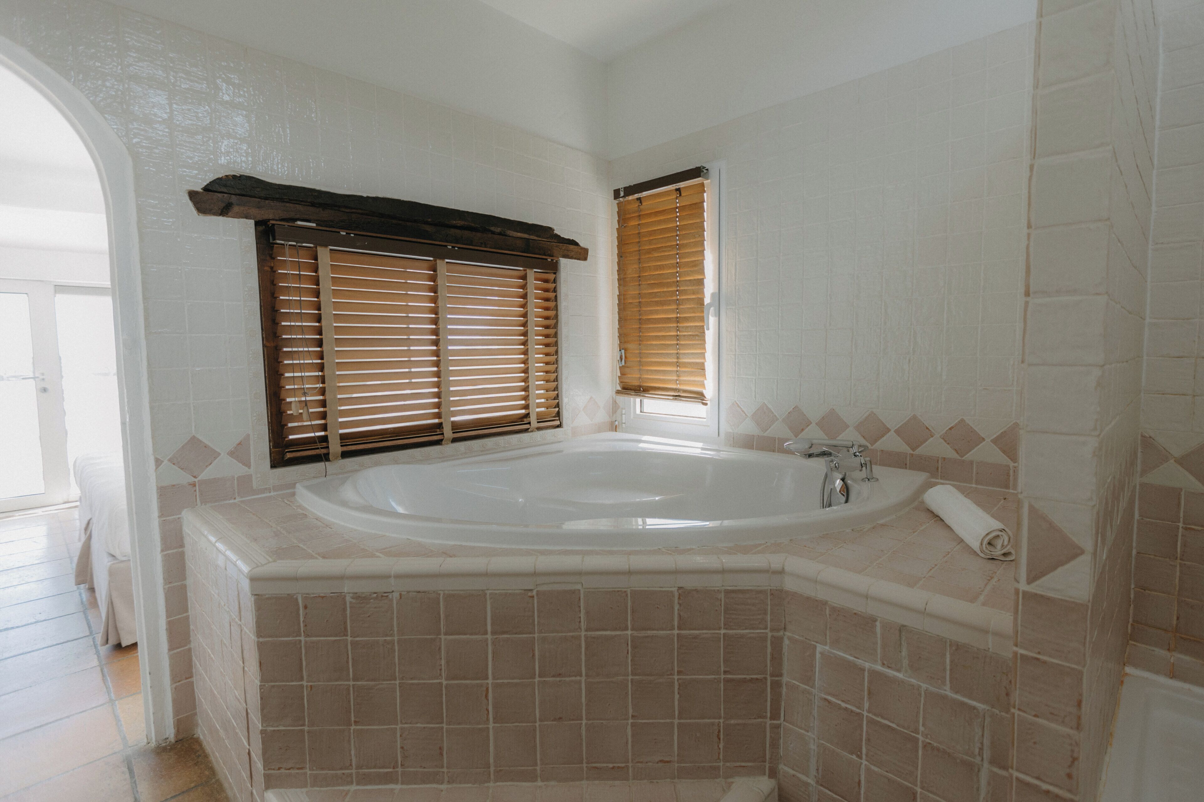 Une salle de bain avec une baignoire, une fenêtre avec des stores et un mur carrelé.