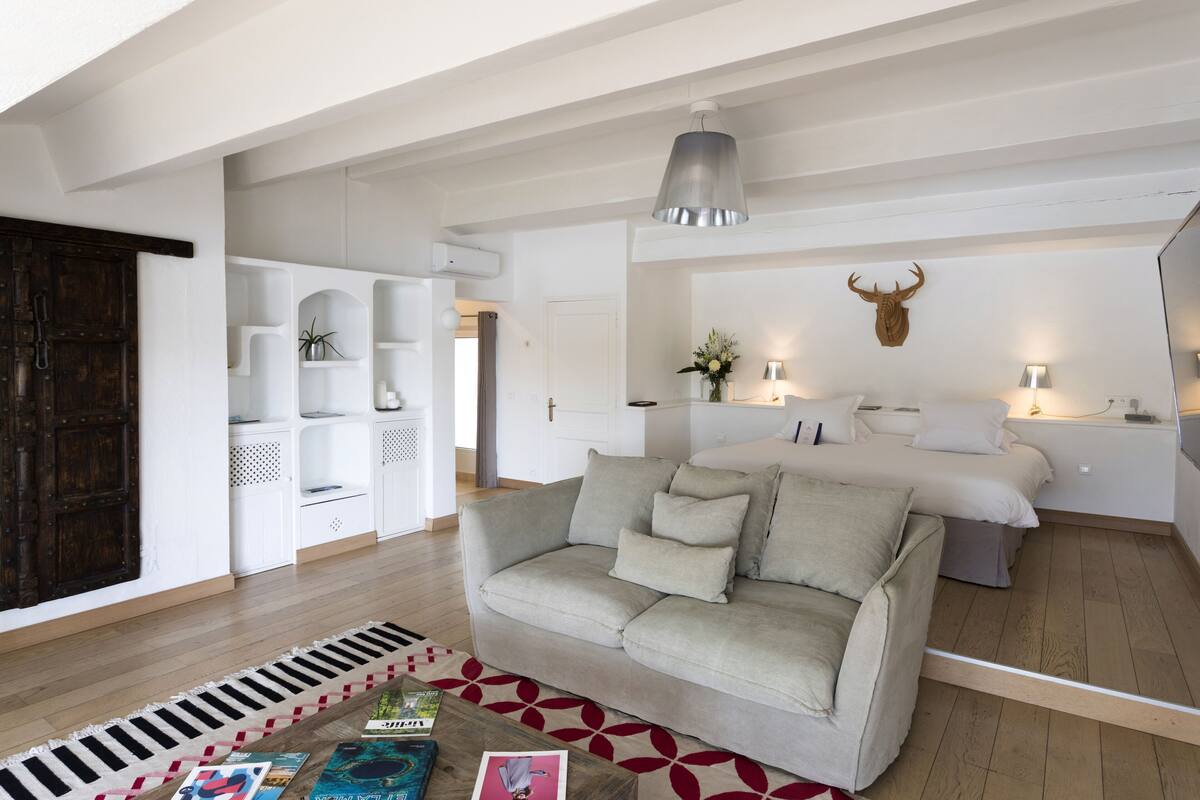 A modern living room with a sofa, a coffee table with magazines, a patterned rug, and a bed with a mounted animal head.