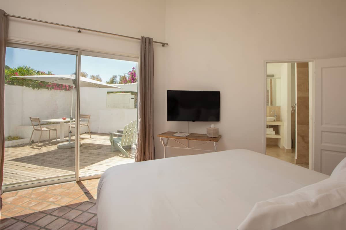 A bedroom with a large bed, a TV on a wooden table, and a sliding glass door leading to an outdoor patio with a table and chairs.