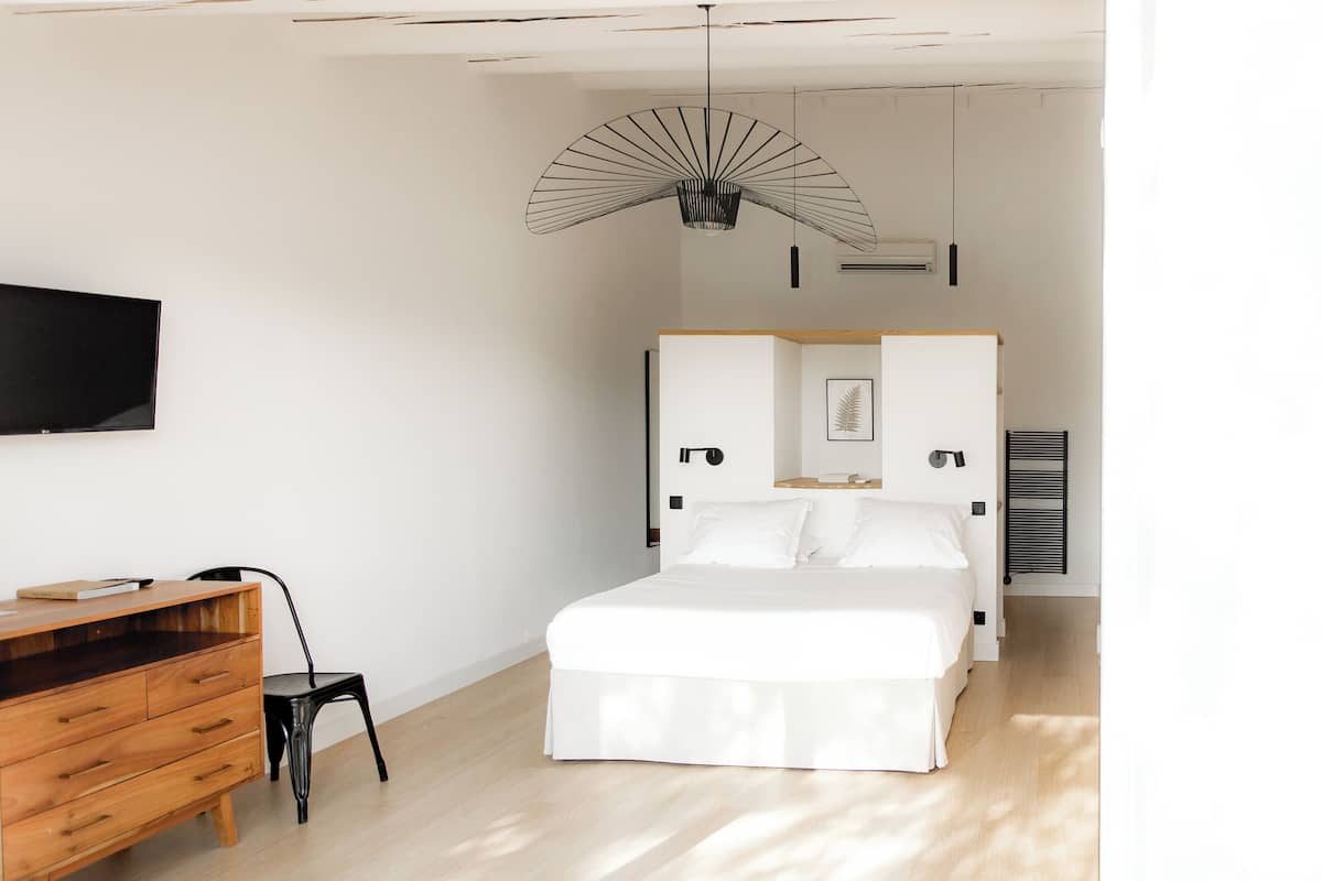 A bedroom with a bed, a wooden dresser, a chair, a TV, and a unique ceiling fan.