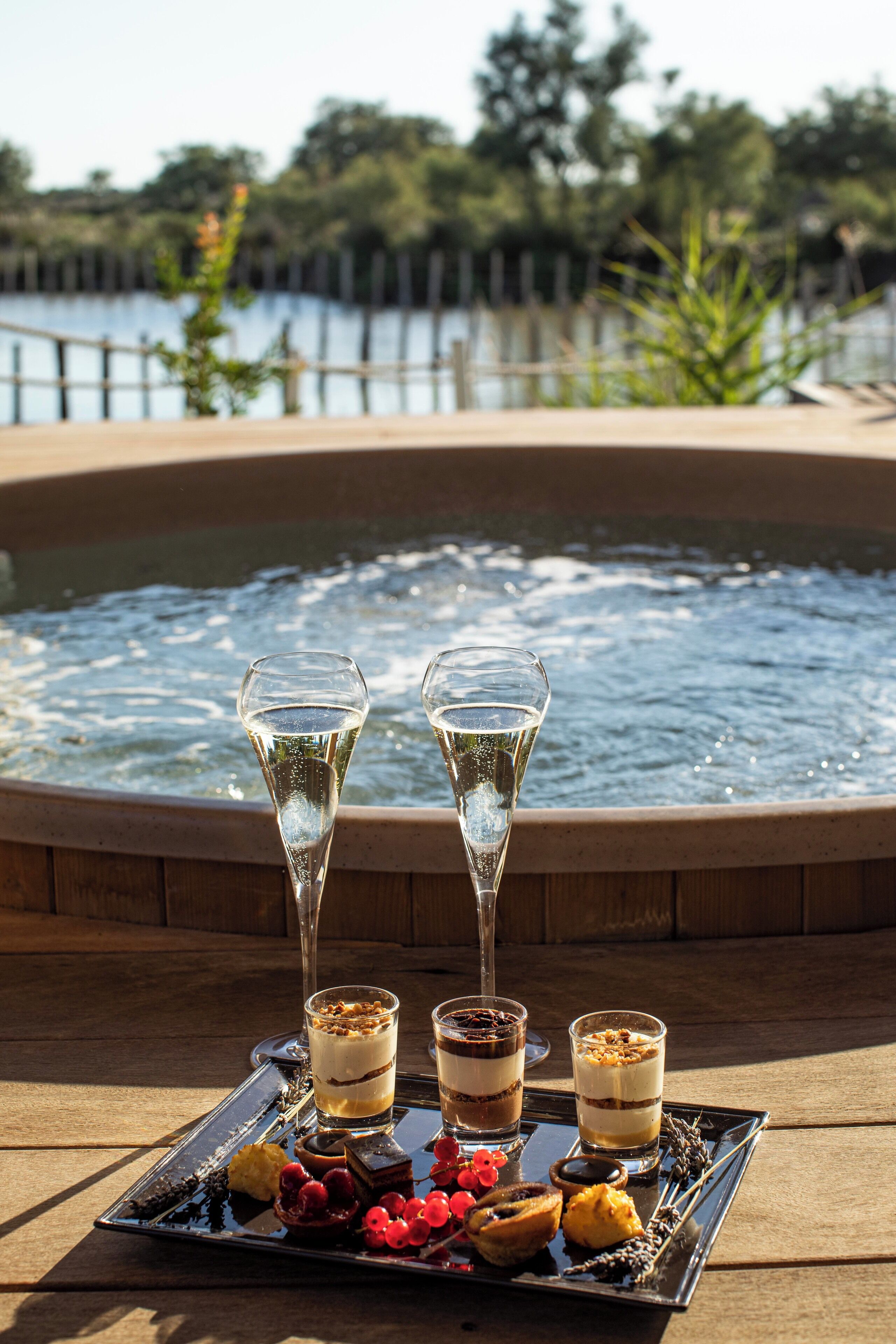 A tray of desserts and champagne glasses by a pool with a wooden deck and a view of a lake.