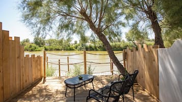 A wooden deck with a table and chairs, overlooking a body of water and surrounded by trees.