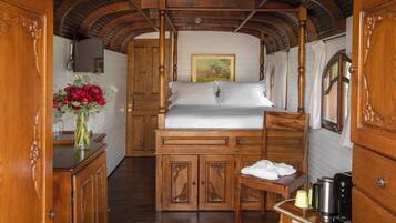 A wooden cabin interior with a bed, a small table with a vase of flowers, and a coffee maker.