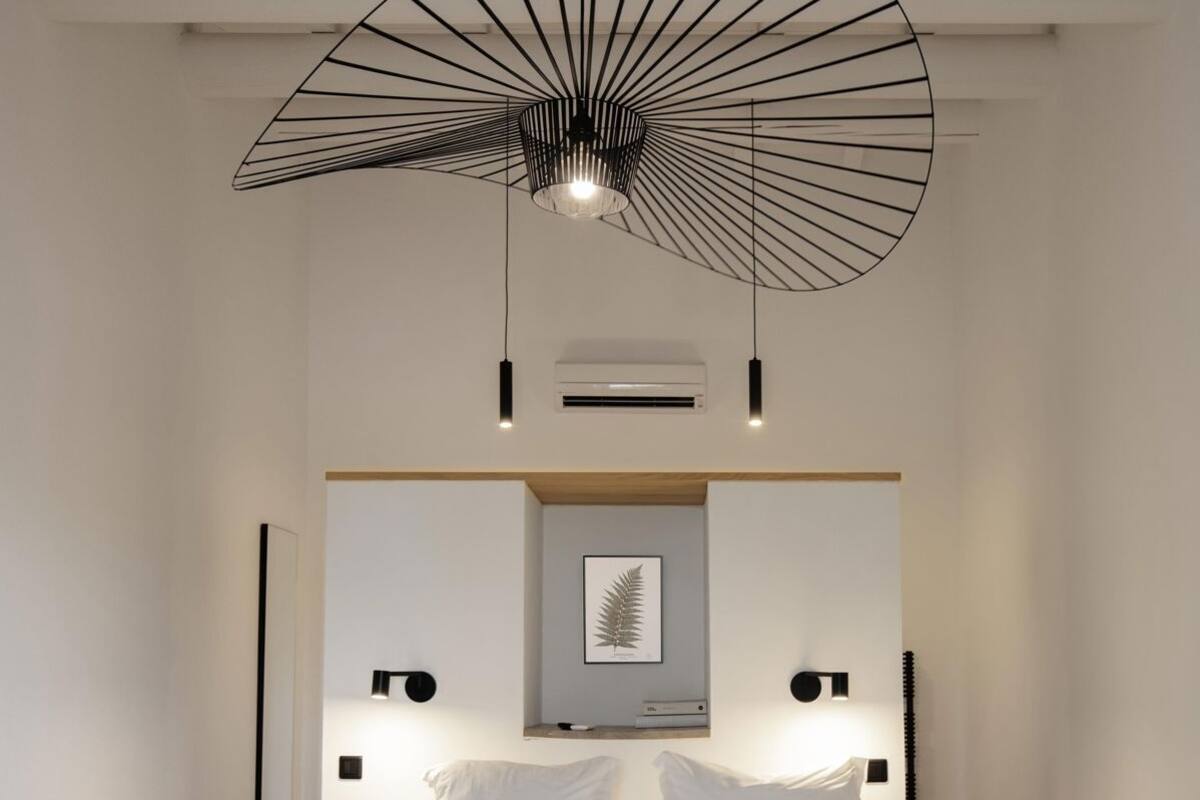 A modern bedroom with a bed, a unique ceiling light, and a wall-mounted air conditioner.