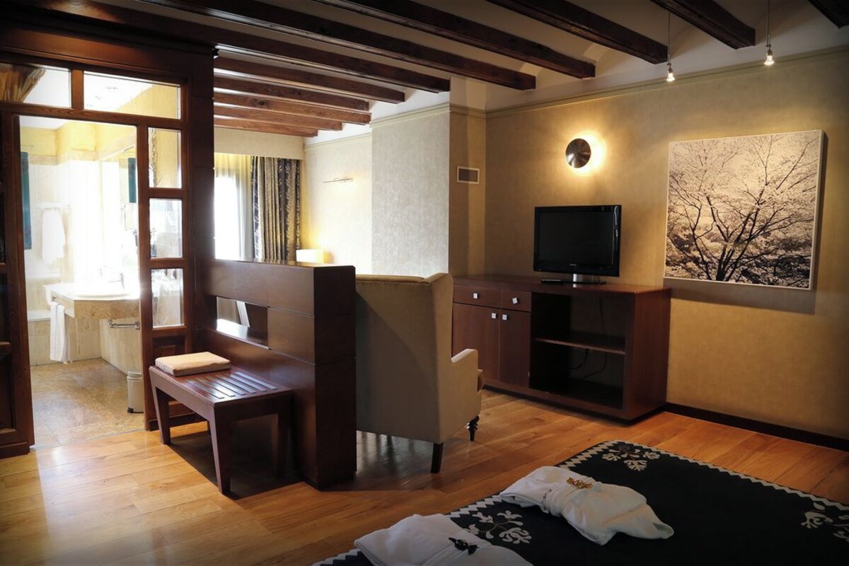 A room with a wooden bench, a television on a cabinet, and a painting on the wall.