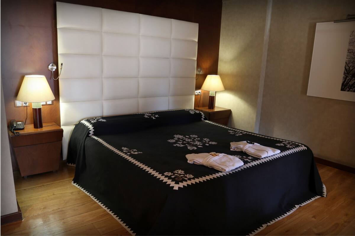 Ein Hotelzimmer mit einem großen Bett, zwei Nachttischlampen, einem Holznachttisch und einem gerahmten Bild an der Wand.