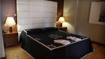 Una habitación de hotel con una cama grande, dos lámparas de noche, una mesita de noche de madera y un cuadro enmarcado en la pared.