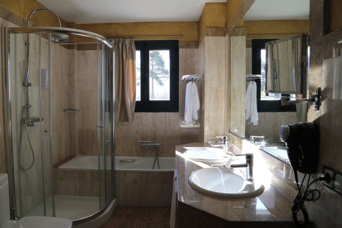 Een badkamer met een douche met glazen wand, een bad, een wastafelmeubel met een wastafel en een haardroger.