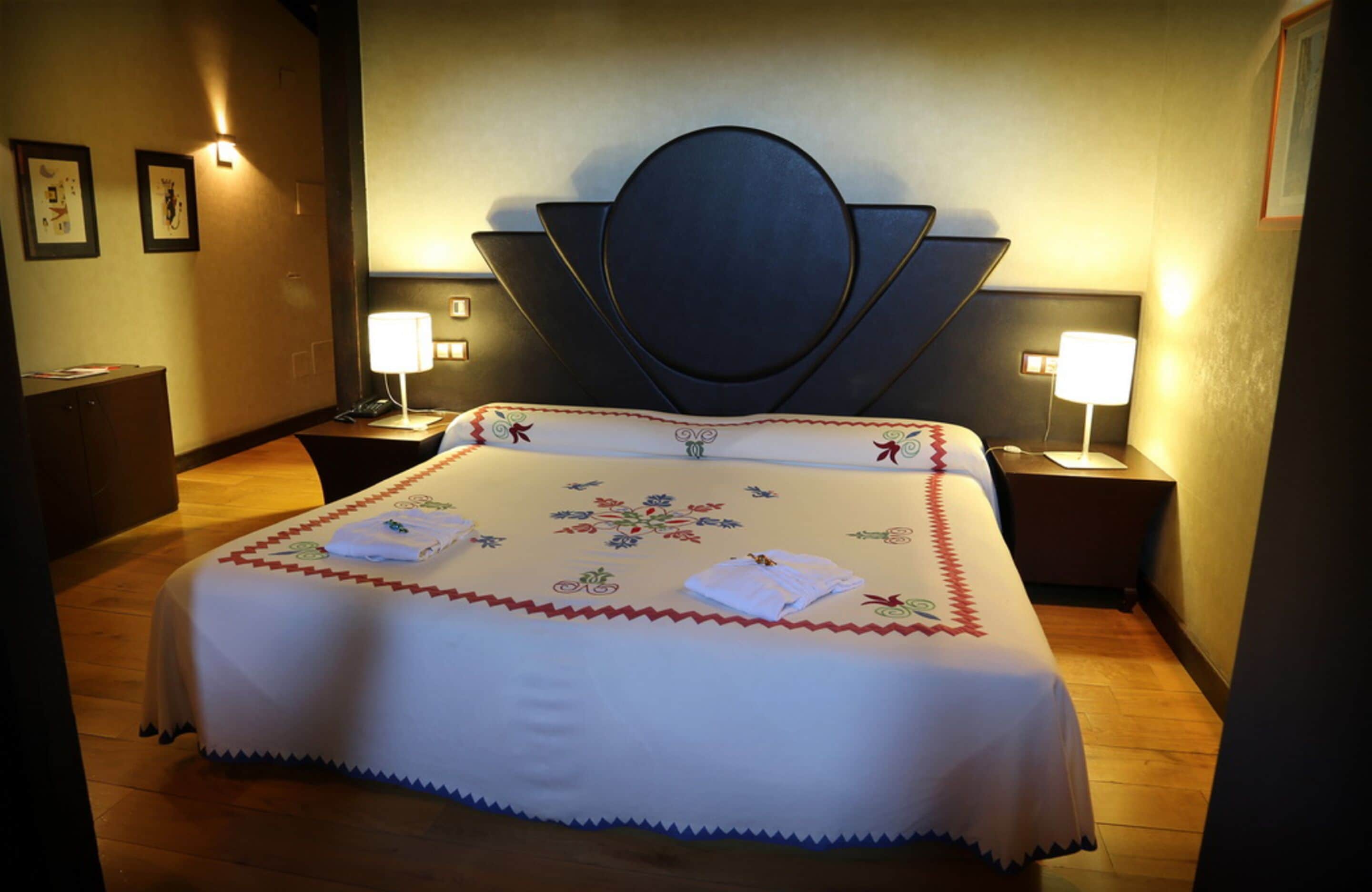 A hotel room with a large bed, two bedside tables with lamps, and a decorative headboard.