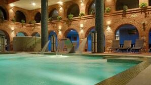 An indoor swimming pool with a brick wall, arched windows, and lounge chairs. - Hotel SPA Abadía de Los Templarios (La Alberca)