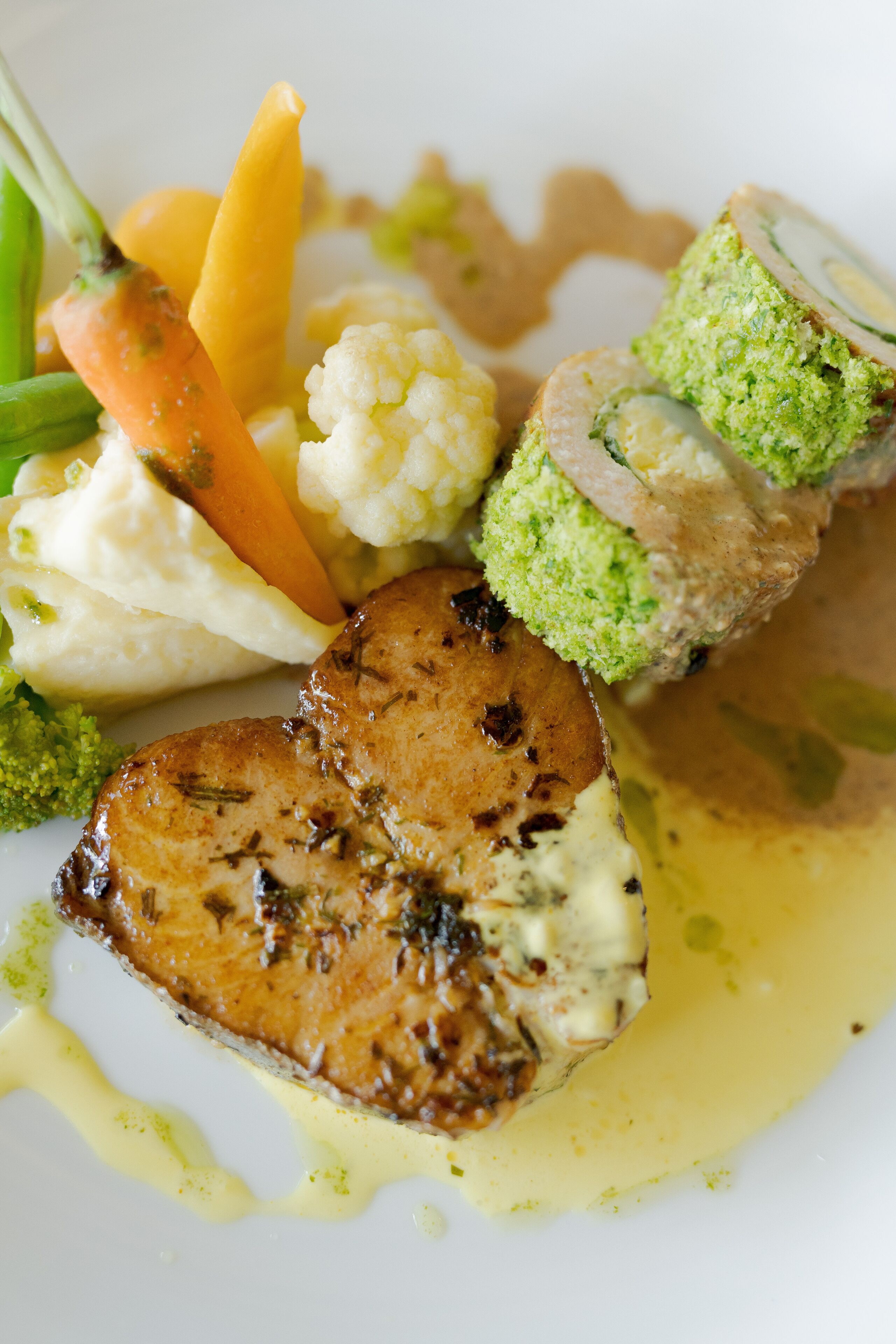 A plate of food with a piece of meat, vegetables, and a green roll.