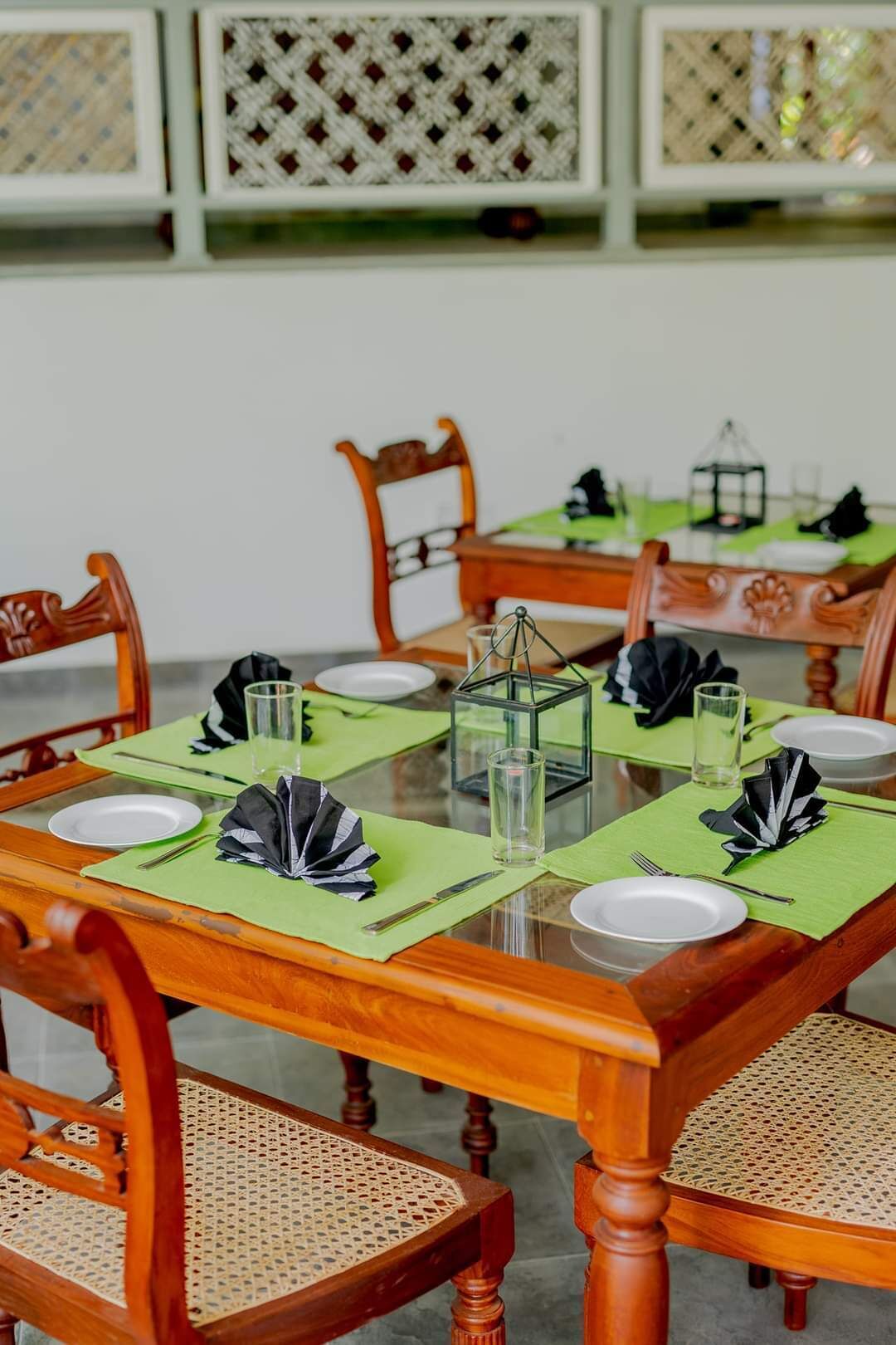 A dining table set with green placemats, white plates, black napkins, and clear glassware.