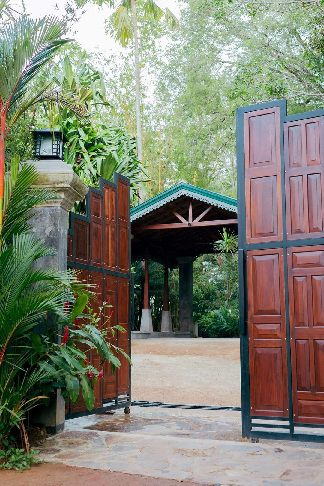 A traditional wooden gate with a covered entrance, surrounded by lush greenery and a stone pathway.