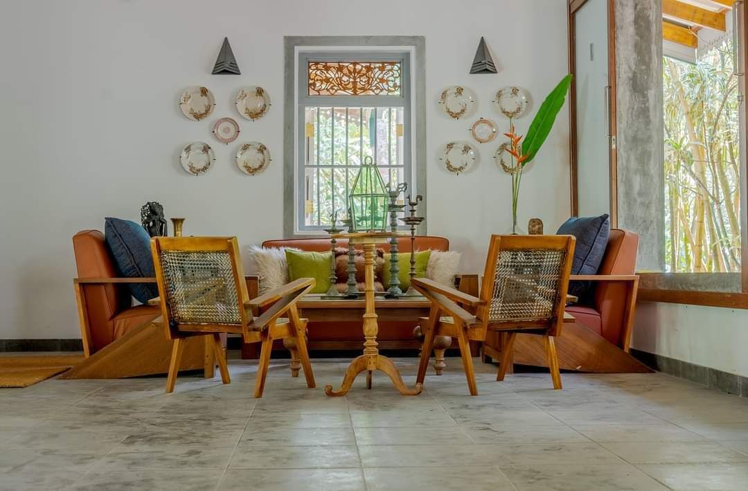 A cozy living room with a wooden coffee table, two wicker chairs, a sofa, and a decorative wall with plates.