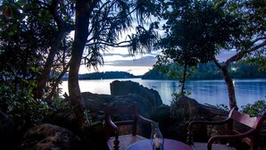 A table and chairs set against a rocky backdrop with a view of a calm lake and distant hills. - Villa Birdlake (Hikkaduwa)