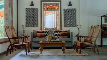 Una sala de estar con un sofá, dos sillas de madera, una mesa de centro y un ventanal con paneles decorativos.