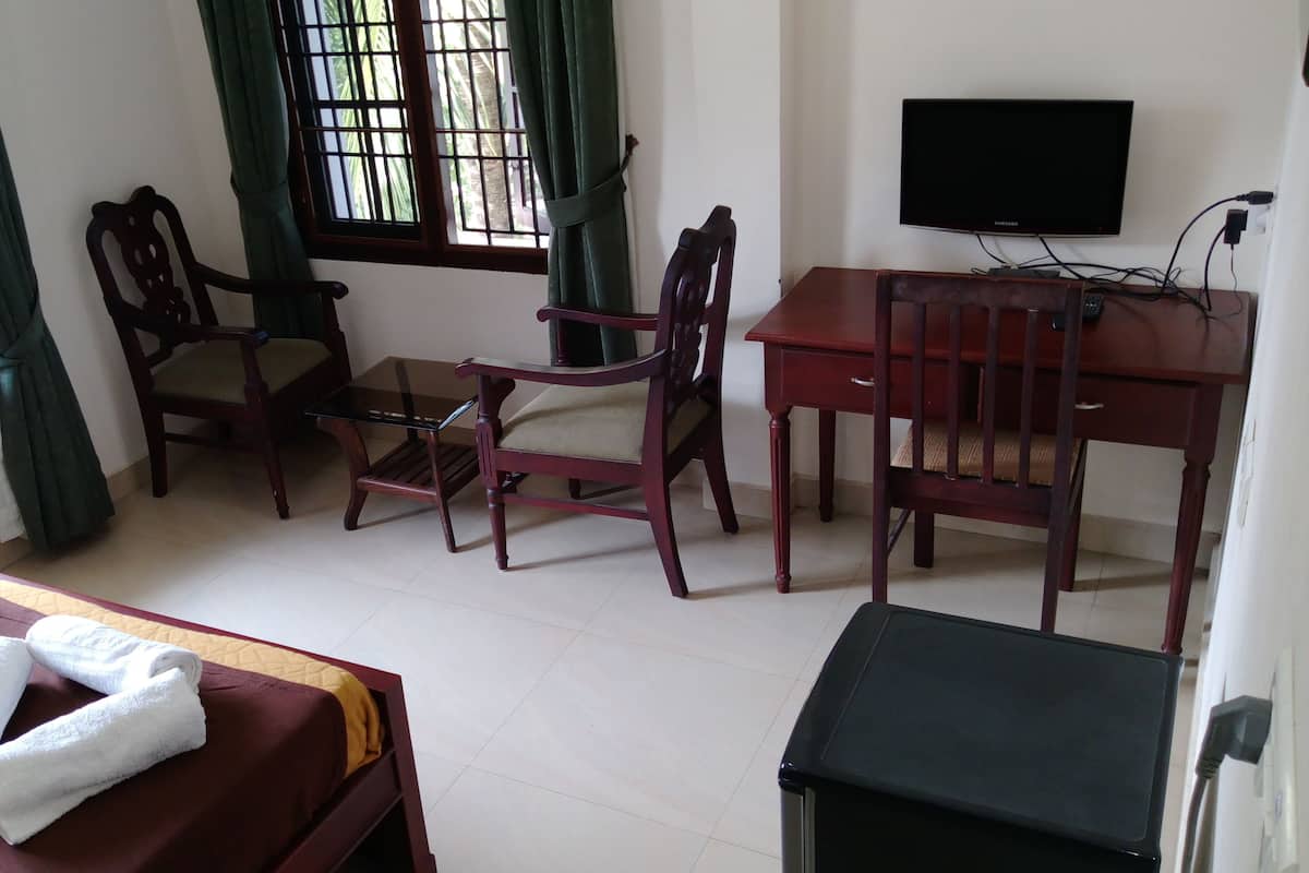 A hotel room with a bed, a desk, two chairs, a television, and a window with curtains.