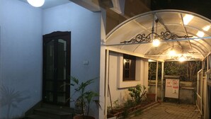 A covered outdoor area with a tiled floor, potted plants, a door, and a small window.