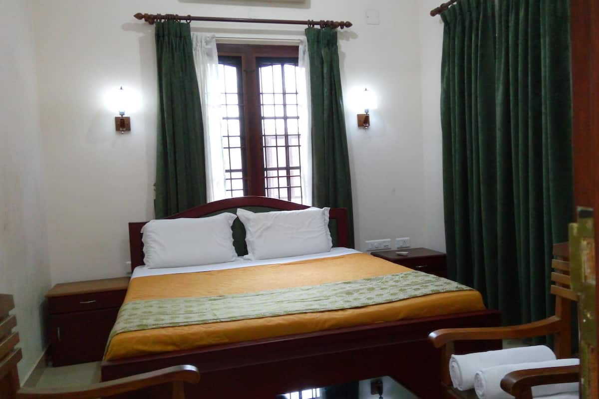 A neatly made bed with a wooden headboard, a bedside table with a lamp, and green curtains.