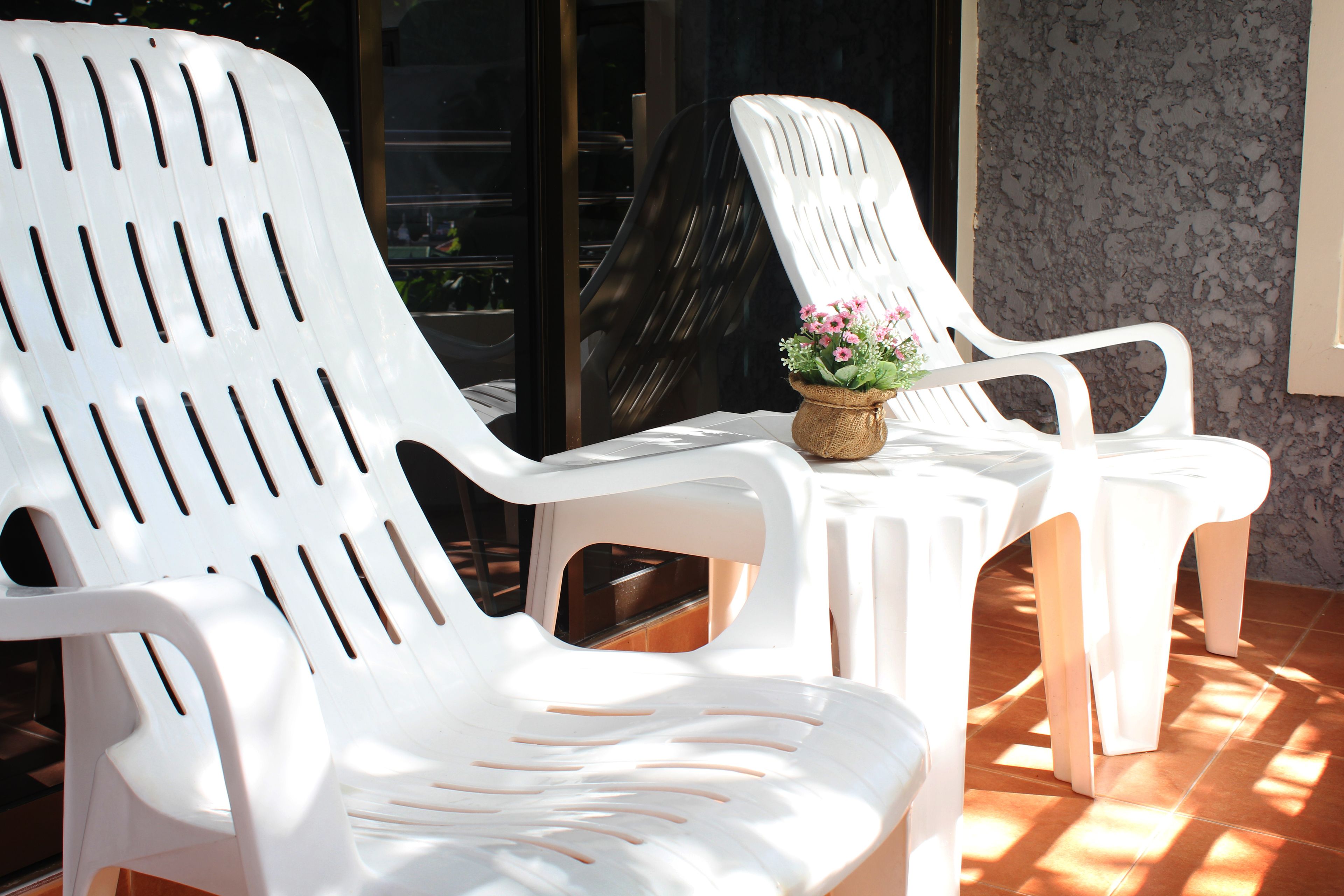 Two white plastic chairs with slatted backrests, a small woven basket with pink flowers, and a tiled floor.