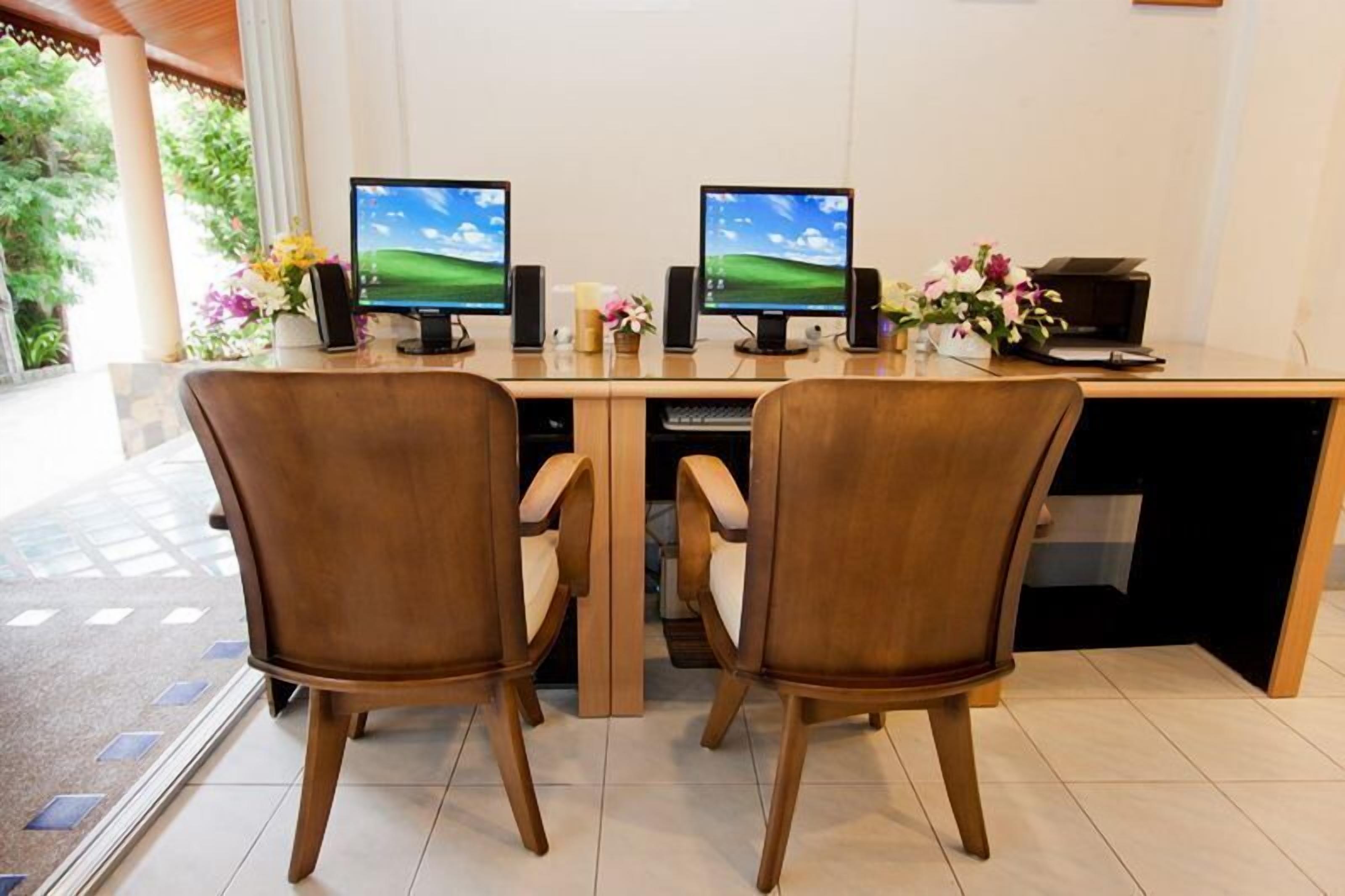 A desk with two monitors, two chairs, a printer, and a vase with flowers.
