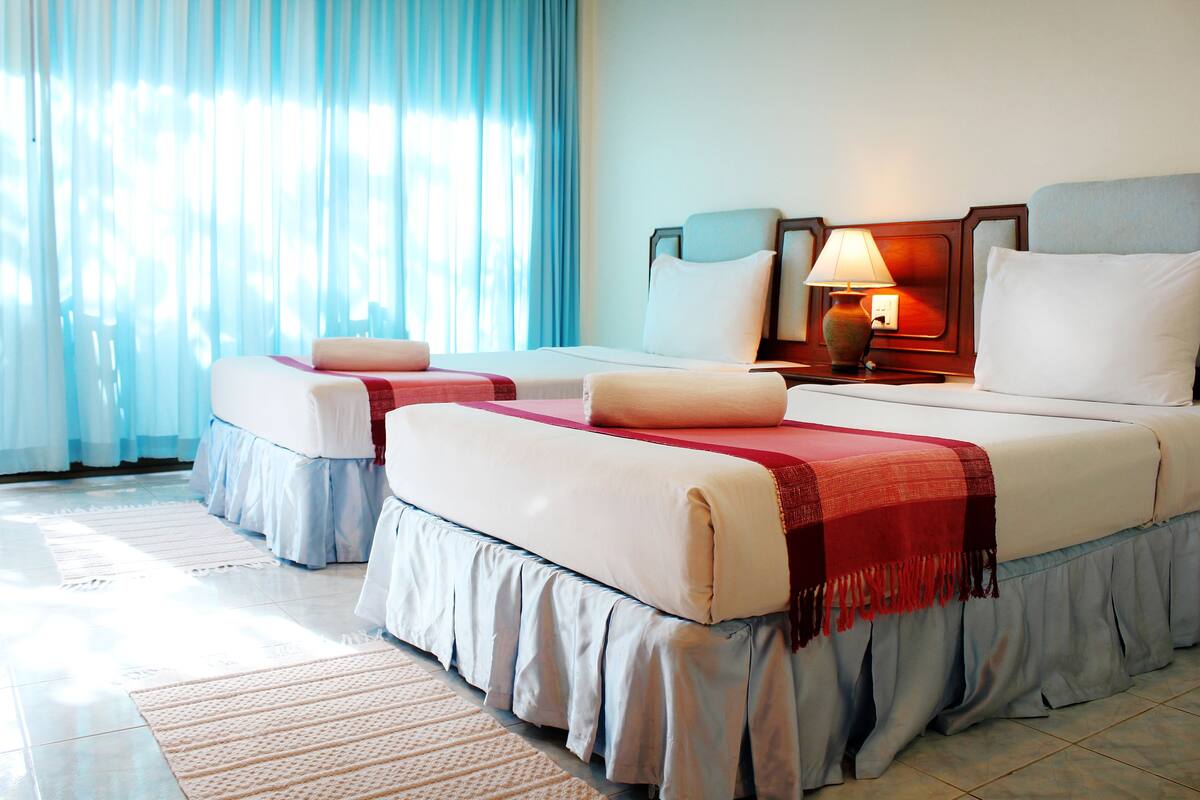 A hotel room with two beds, a nightstand with a lamp, and a window with curtains.