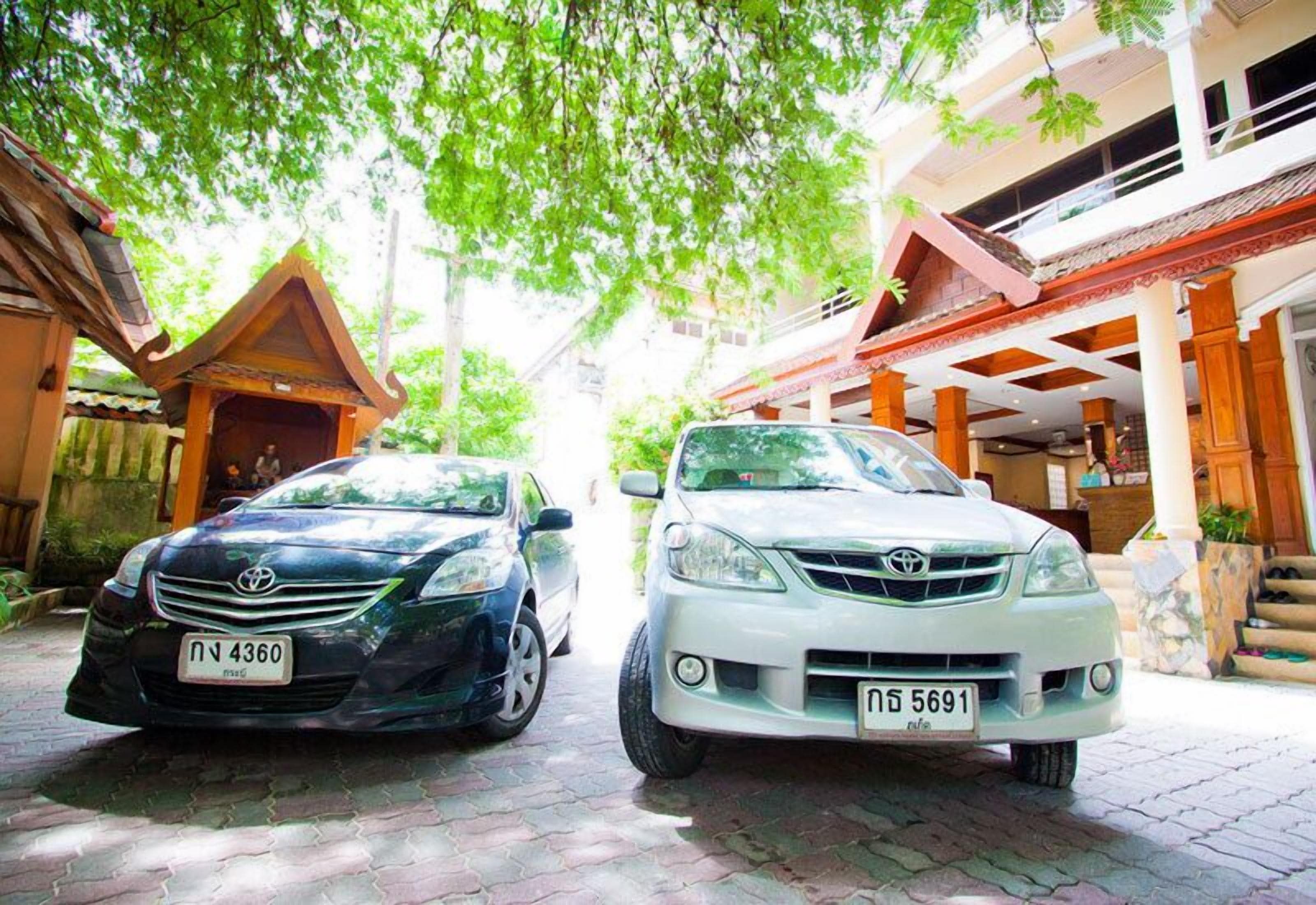 Dos coches estacionados frente a un edificio de estilo arquitectónico tradicional, con un porche y una escalera que conduce a un segundo piso.