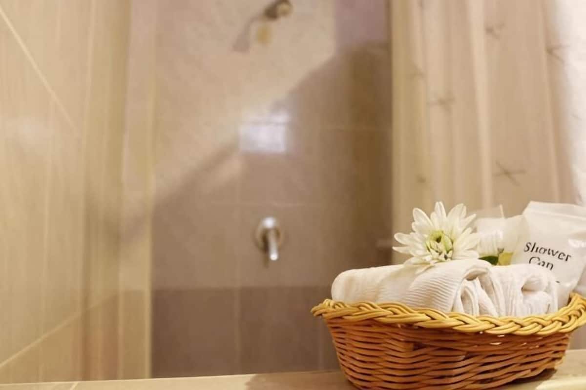 A bathroom with a shower curtain, a wicker basket with towels, and a flower.