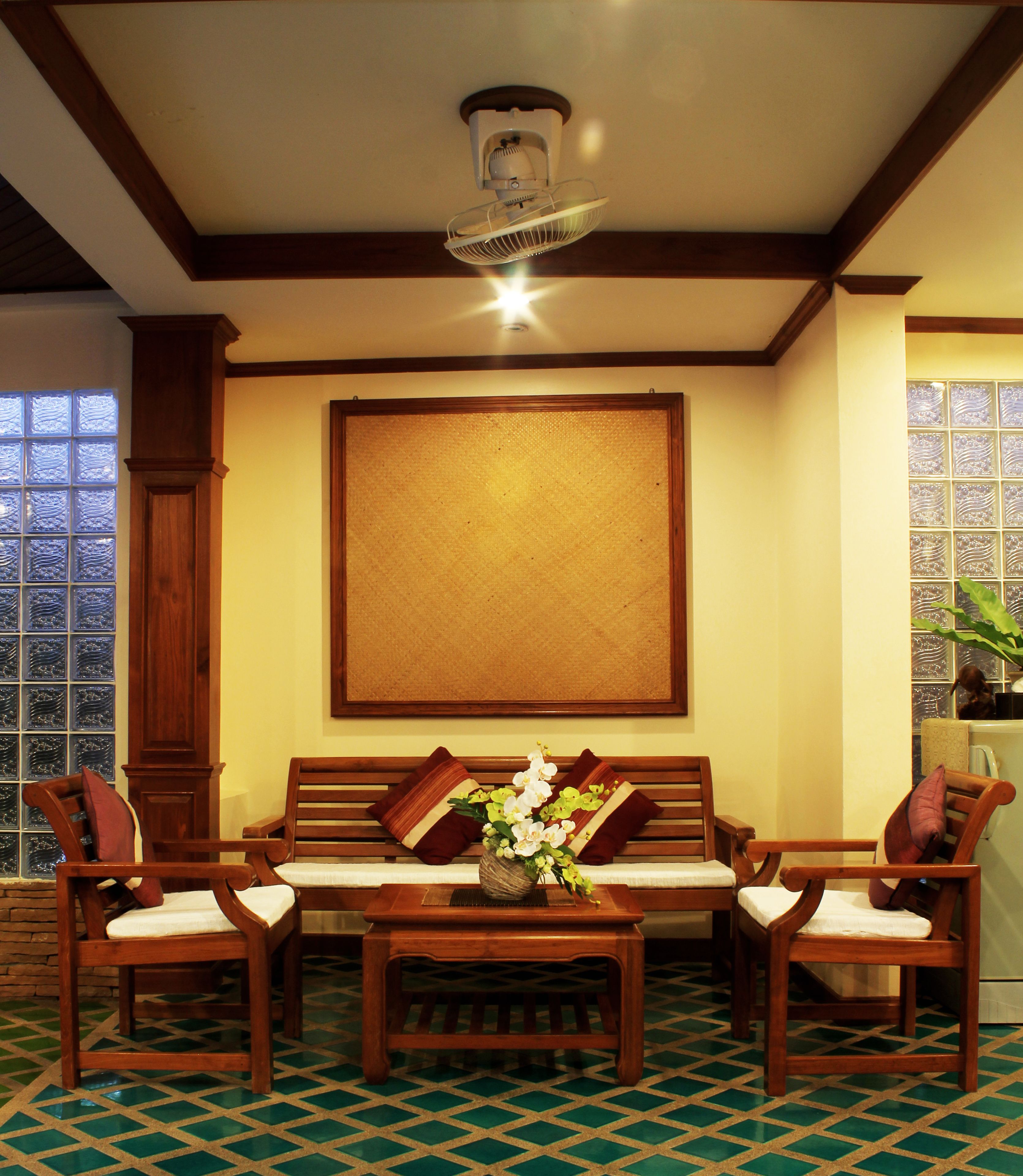 A room with a wooden bench, two chairs, a small table with a vase of flowers, a ceiling fan, and a large window with a view.