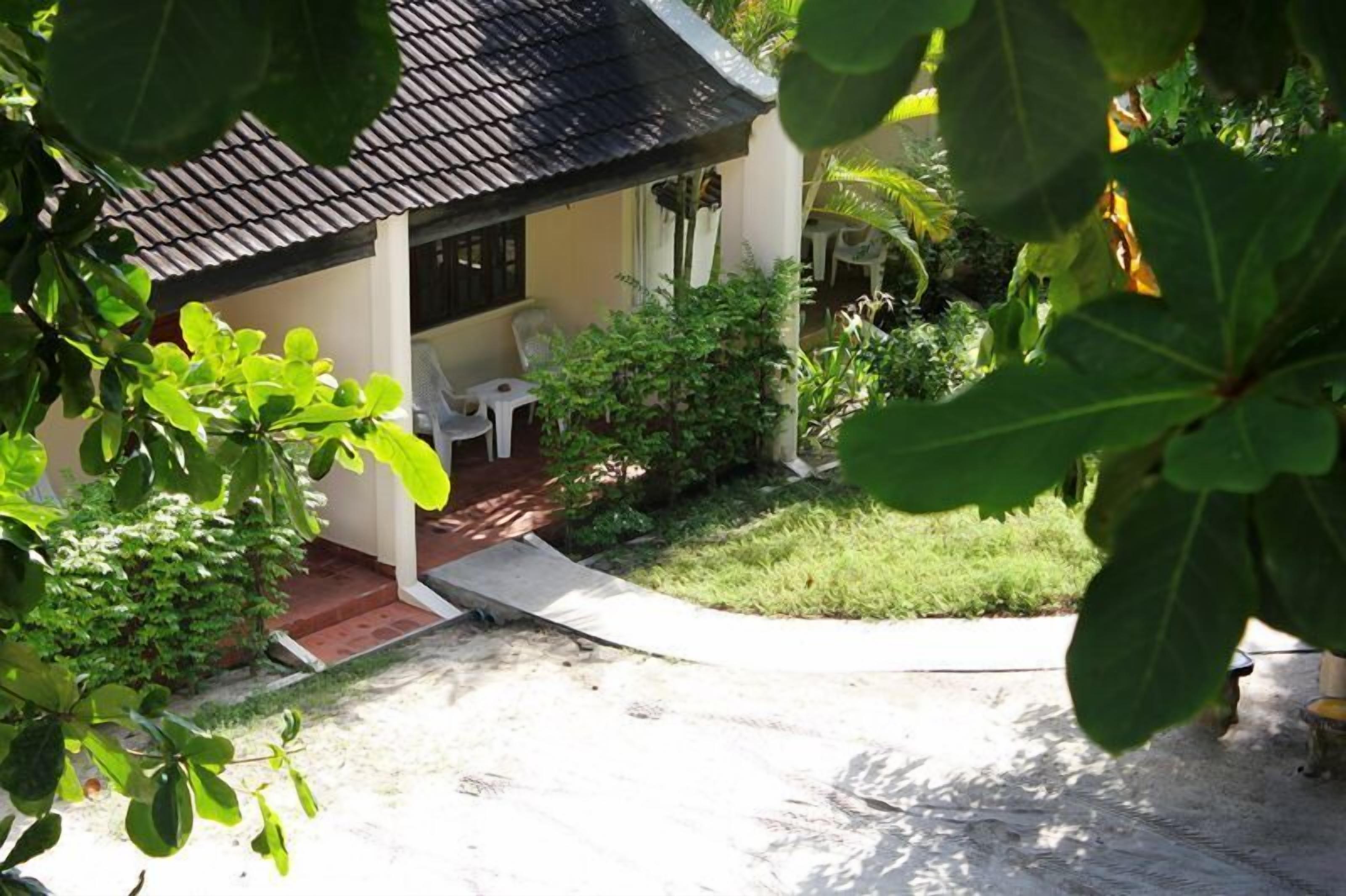 Una casa con techo de tejas, un porche cubierto y un pequeño jardín con una silla y una mesa.