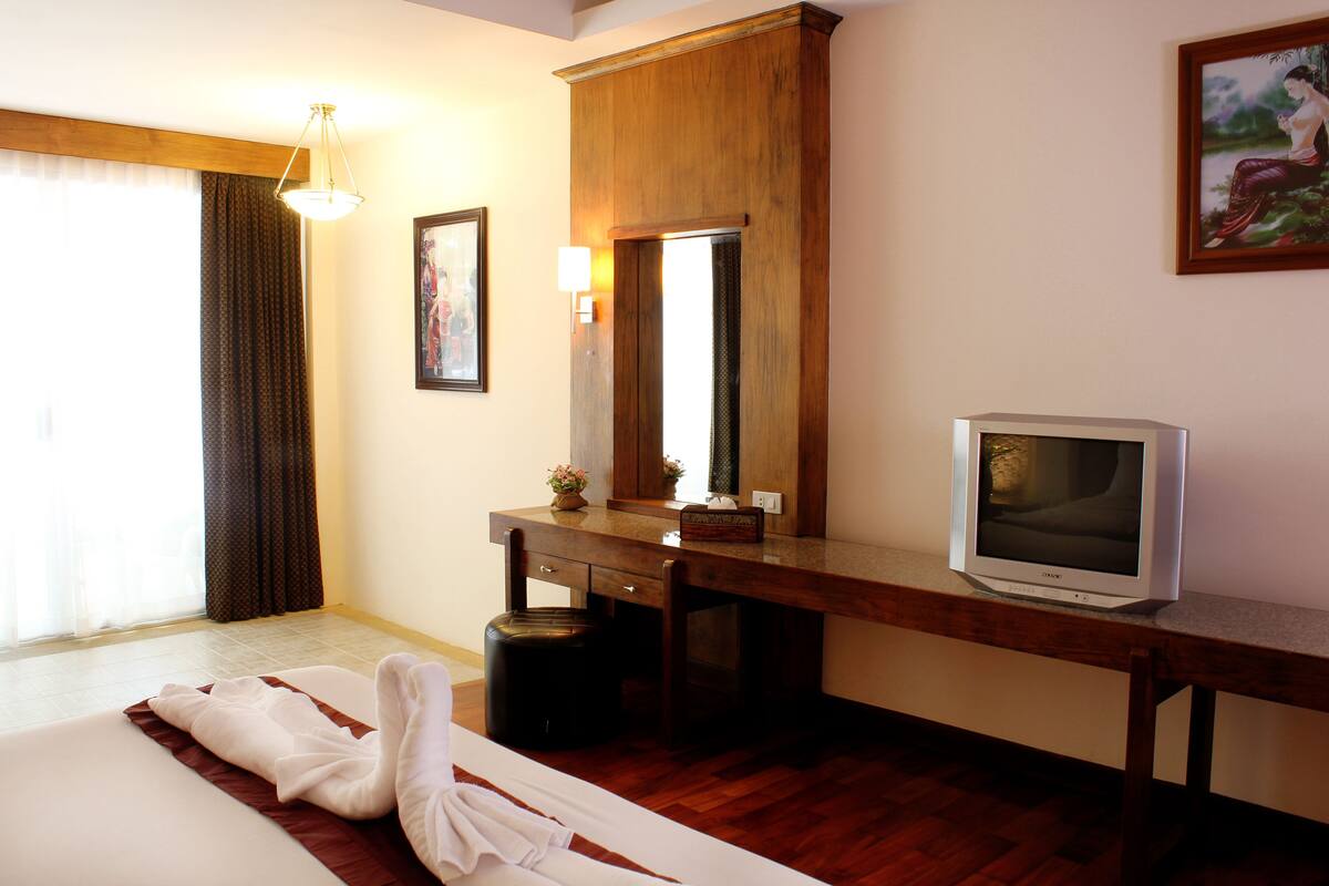 A hotel room with a bed, a desk, a television, and a window with curtains.
