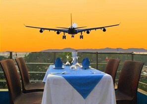 A table set for dining with a view of an airplane landing. - Air Inn (Dhaka)