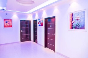 Un pasillo con tres puertas, cada una con una placa de número, y un cuadro en la pared.