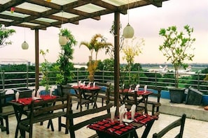An outdoor dining area with tables set for two, surrounded by greenery and a view of the cityscape. - Air Inn (Dhaka)