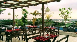 An outdoor seating area with tables and chairs, surrounded by greenery and a view of an airport in the distance. - Air Inn (Dhaka)